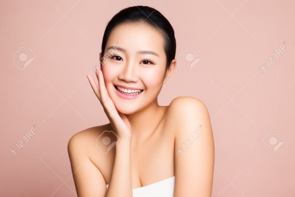 Schönes Gesicht. Lächelnde asiatische Frau, die gesundes Hautporträt berührt. Schönes glückliches Mädchenmodell mit frisch leuchtender, hydratisierter Gesichtshaut und natürlichem Make-up auf weißem Hintergrund,