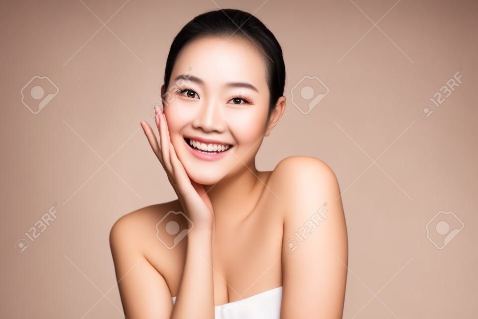 Schönes Gesicht. Lächelnde asiatische Frau, die gesundes Hautporträt berührt. Schönes glückliches Mädchenmodell mit frisch leuchtender, hydratisierter Gesichtshaut und natürlichem Make-up auf weißem Hintergrund,