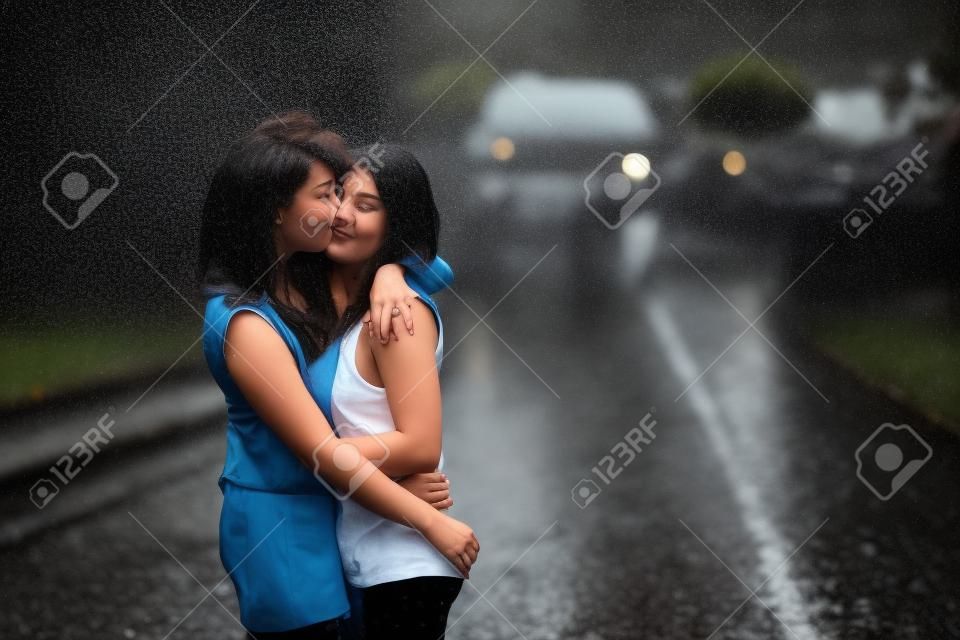 Lesbiche ragazze baciano sotto la pioggia battente. Hanno ottenuto bagnato.