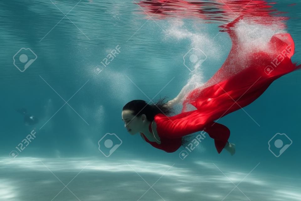 赤いドレスを着た女性は、プール内の水の下にダイブします。