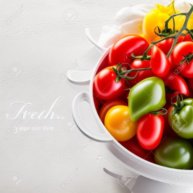 Assorted colorful tomatoes and vegetables in colander on white background - healthy eating concept (with easy removable sample text)