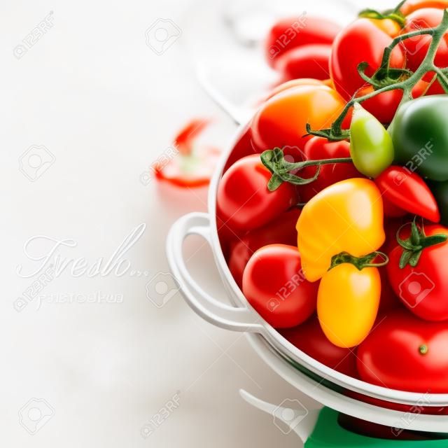 Assorted colorful tomatoes and vegetables in colander on white background - healthy eating concept (with easy removable sample text)