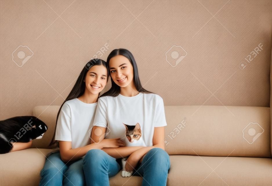 Mãe e filha estão sentadas no sofá com os braços em volta uma da outra segurando um gato.