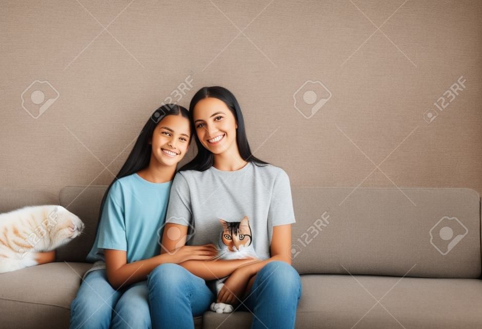 mutter und tochter sitzen auf der couch mit ihren armen umeinander und halten eine katze.