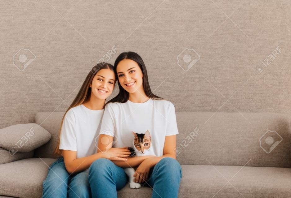 mamma e figlia sono sedute sul divano con le braccia l'una intorno all'altra e tengono un gatto.