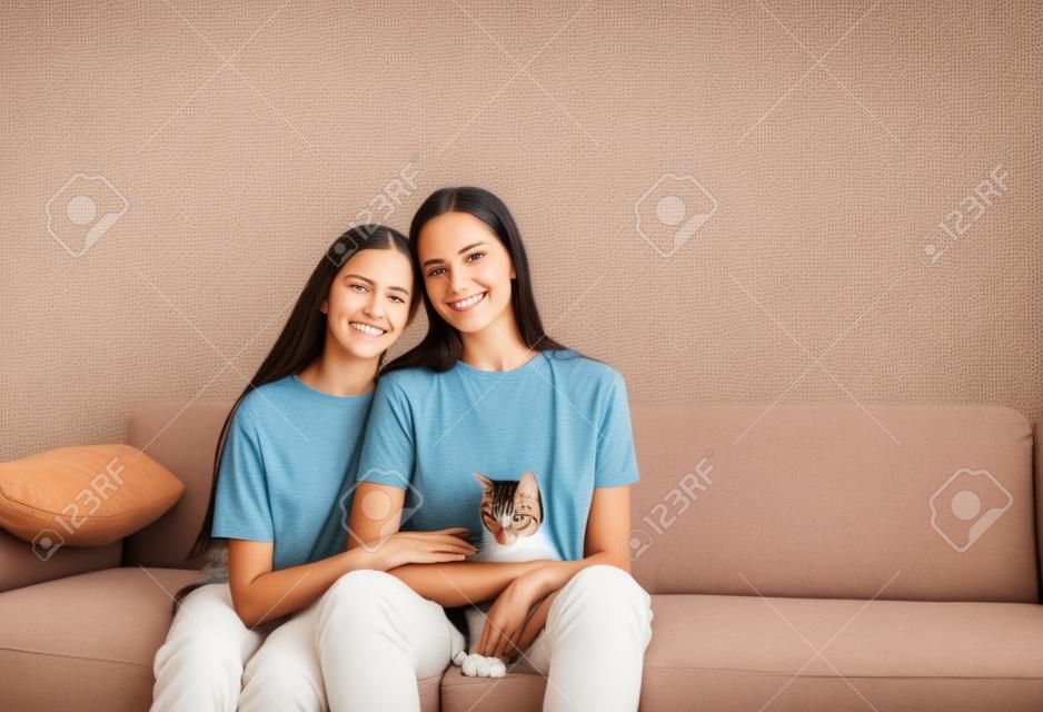 mom and daughter are sitting on the couch with their arms around each other holding a cat.