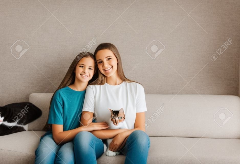 mutter und tochter sitzen auf der couch mit ihren armen umeinander und halten eine katze.