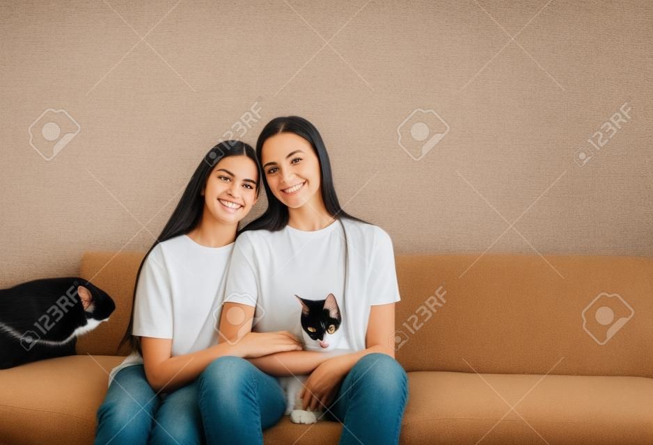 mom and daughter are sitting on the couch with their arms around each other holding a cat.