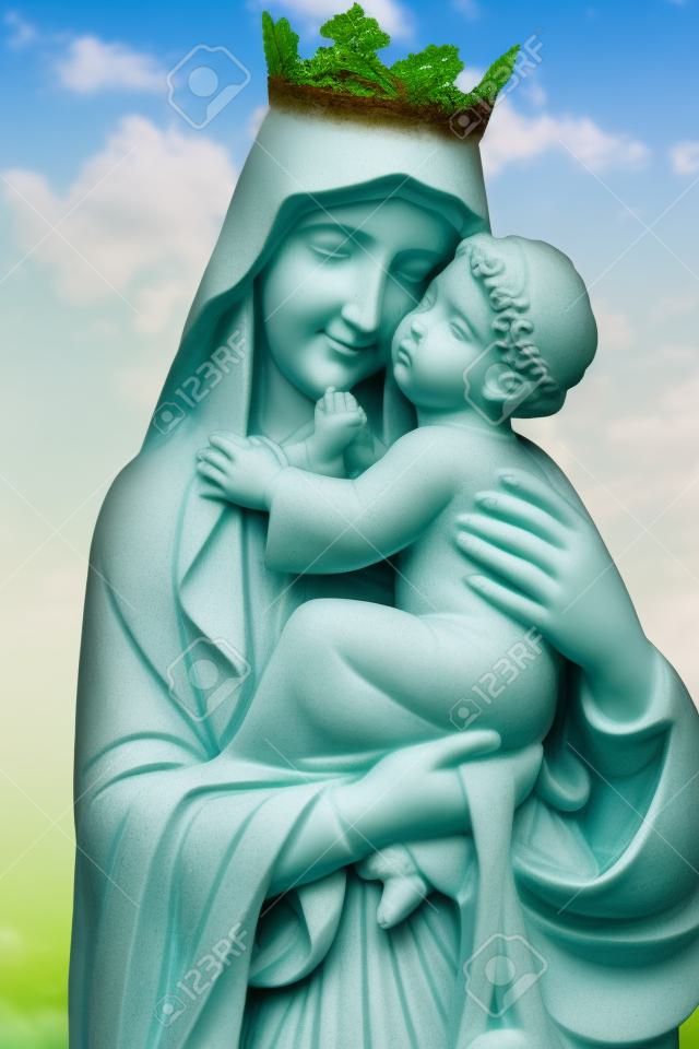 Statue de la vierge Marie portant l'enfant Jésus avec un fond de végétation diffuse