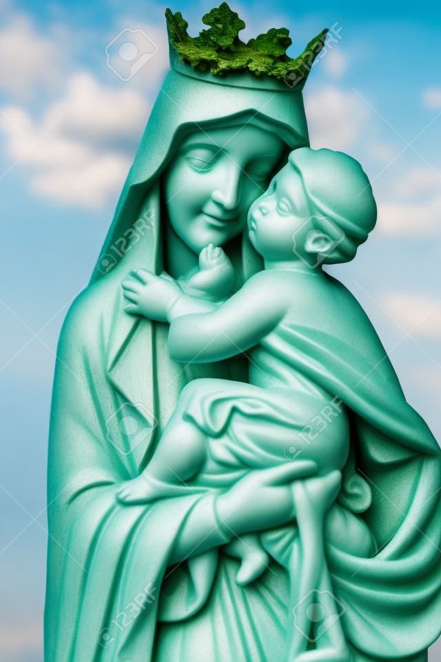 Statue de la vierge Marie portant l'enfant Jésus avec un fond de végétation diffuse