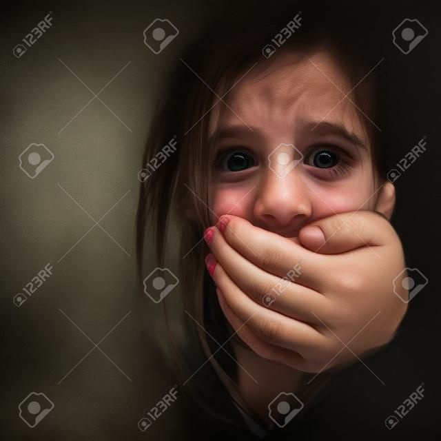 Portrait d'une petite fille effrayée maltraité par un homme adulte qui couvre sa bouche avec sa main que sa main est visible, le reste est caché dans les ombres