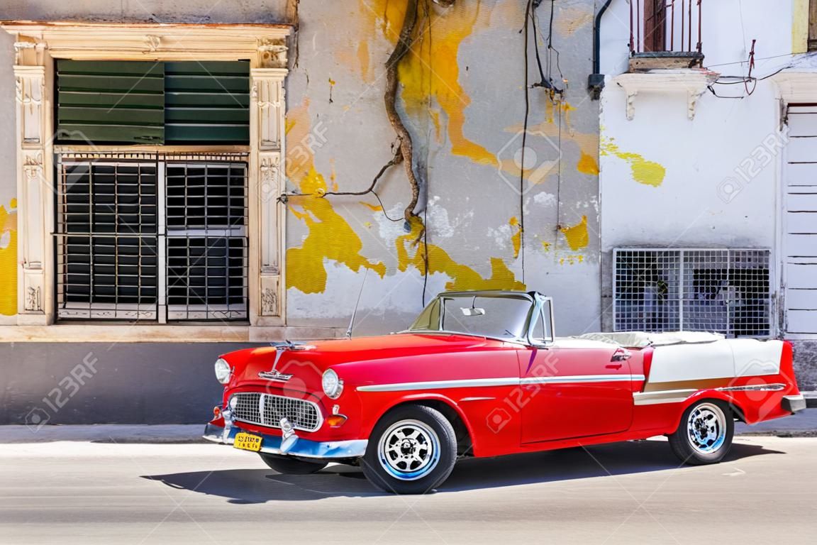 Klassieke rode cabriolet naast een sjofel gebouw in Old Havana