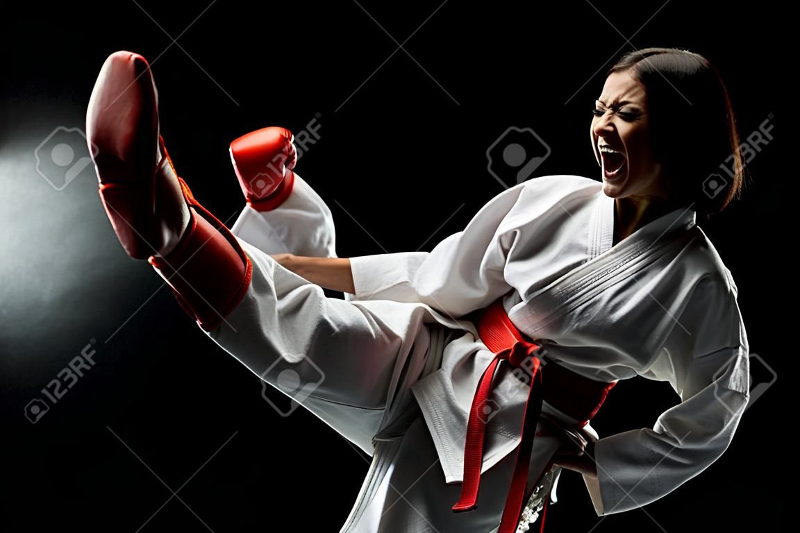 Mädchen, das Karate-Beintritt ausübt und vor schwarzem Hintergrund schreit