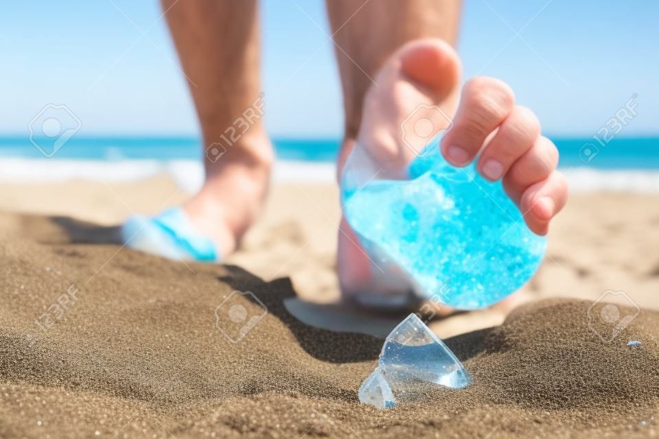 男人去海灘，踩著碎玻璃瓶的碎片一個，這是躺在與惡劣環境的地方散落的沙子上的風險