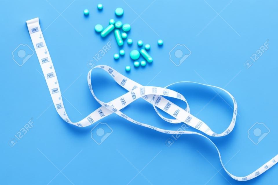 Pills and centimeter tape on a blue background. Weight loss concept. Choice problems, sports and healthy lifestyle or medicines.