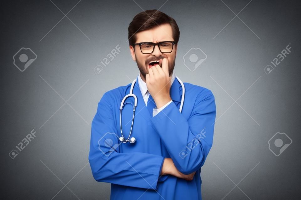 Médico masculino inseguro mordendo as unhas parecendo engraçado com medo desejando algo ansioso.