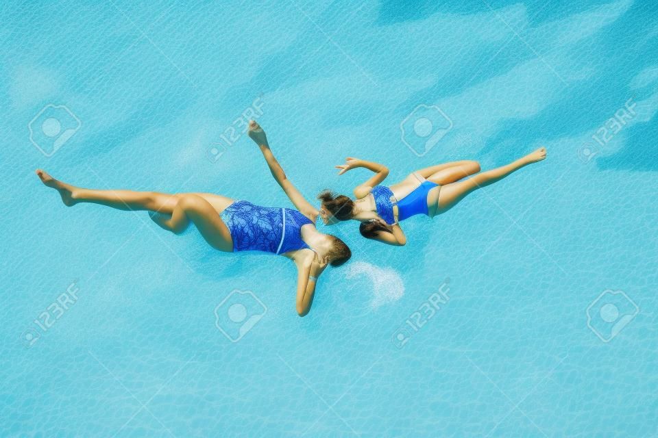 Zwei Mädchen im Badeanzug haben Spaß am Gras am Pool im Sommer