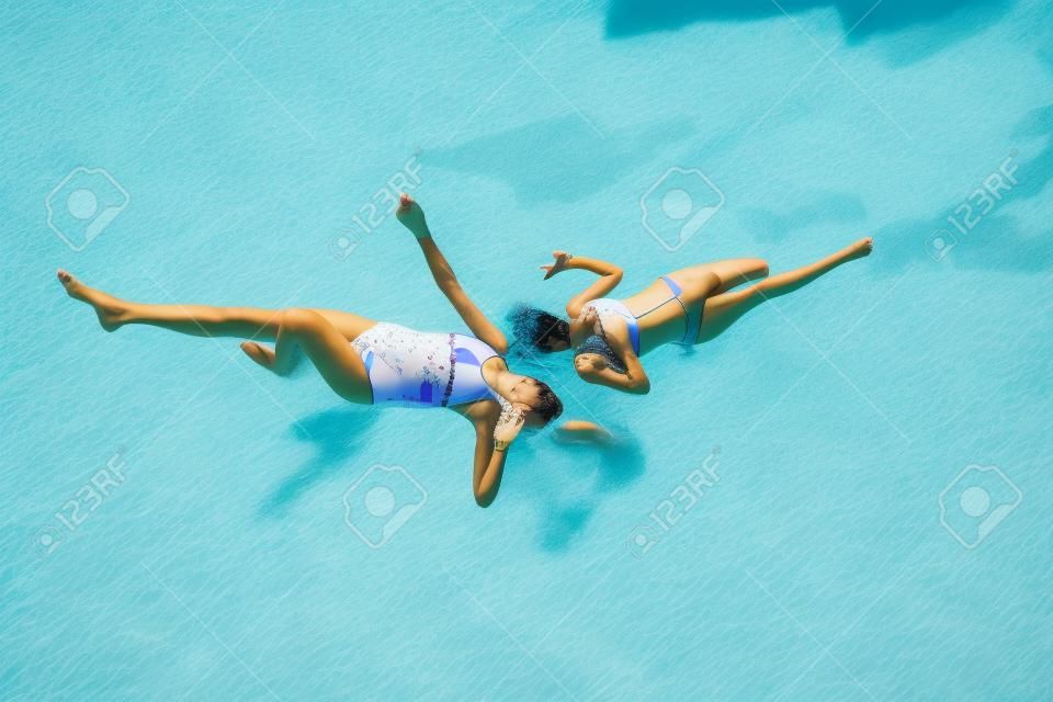 Zwei Mädchen im Badeanzug haben Spaß am Gras am Pool im Sommer