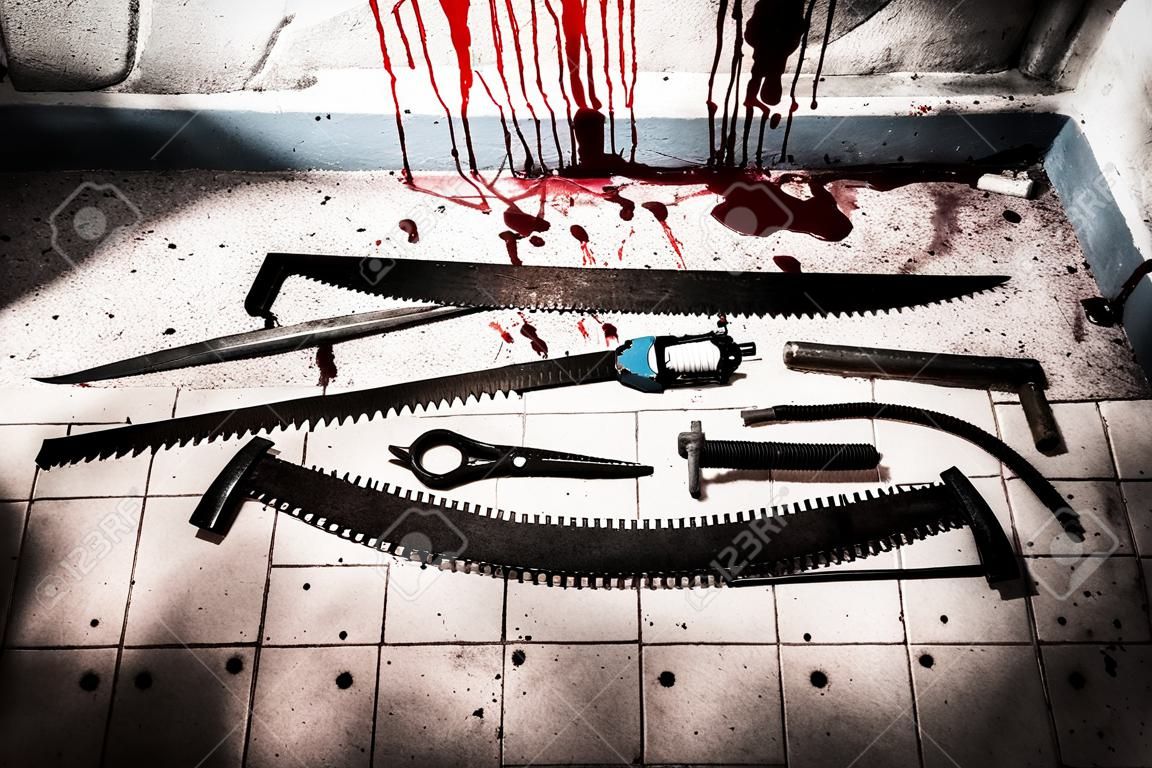Des scies, des faucilles, des pinces et d'autres dispositifs sur le sol sanglant au sous-sol avec des tuyaux et des fils dans un concept d'horreur de Halloween