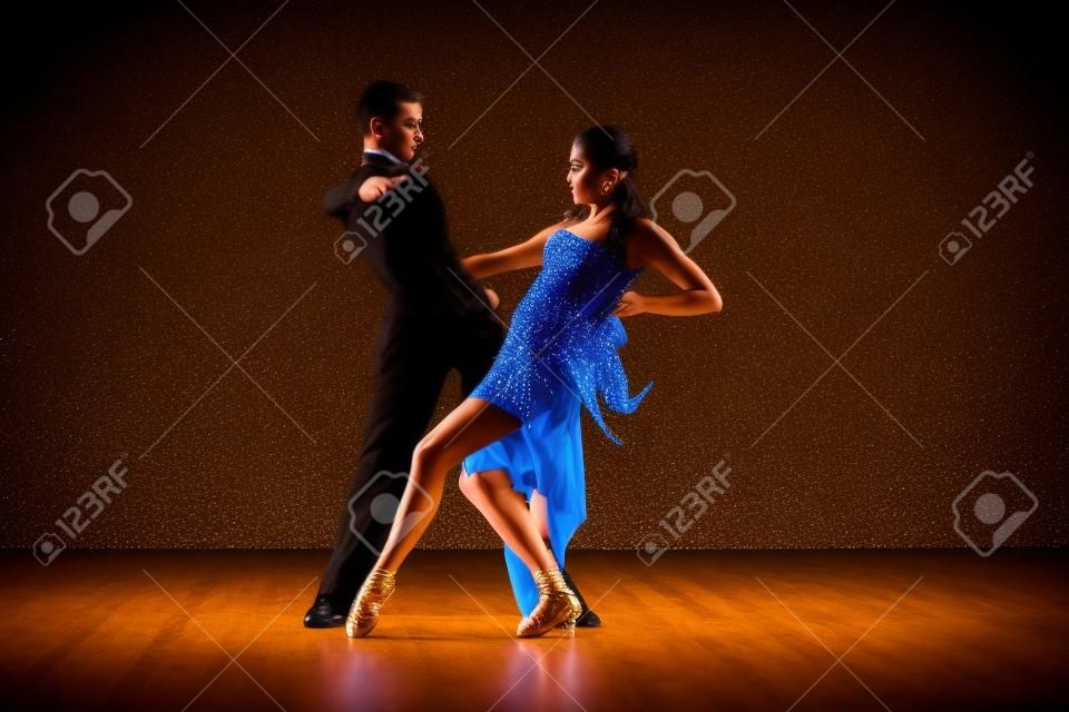 Latino dancers in ballroom against on black 