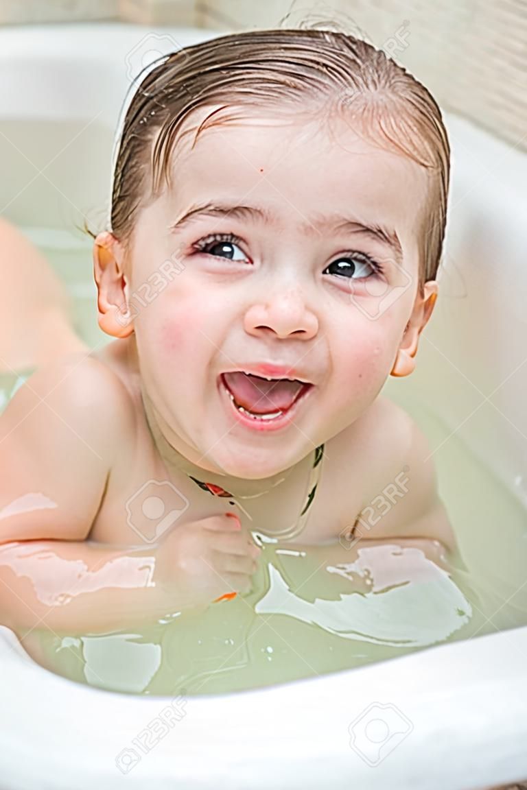 Ein kleines Mädchen macht lustige Gesichter in der Badewanne und sie ist sehr glücklich