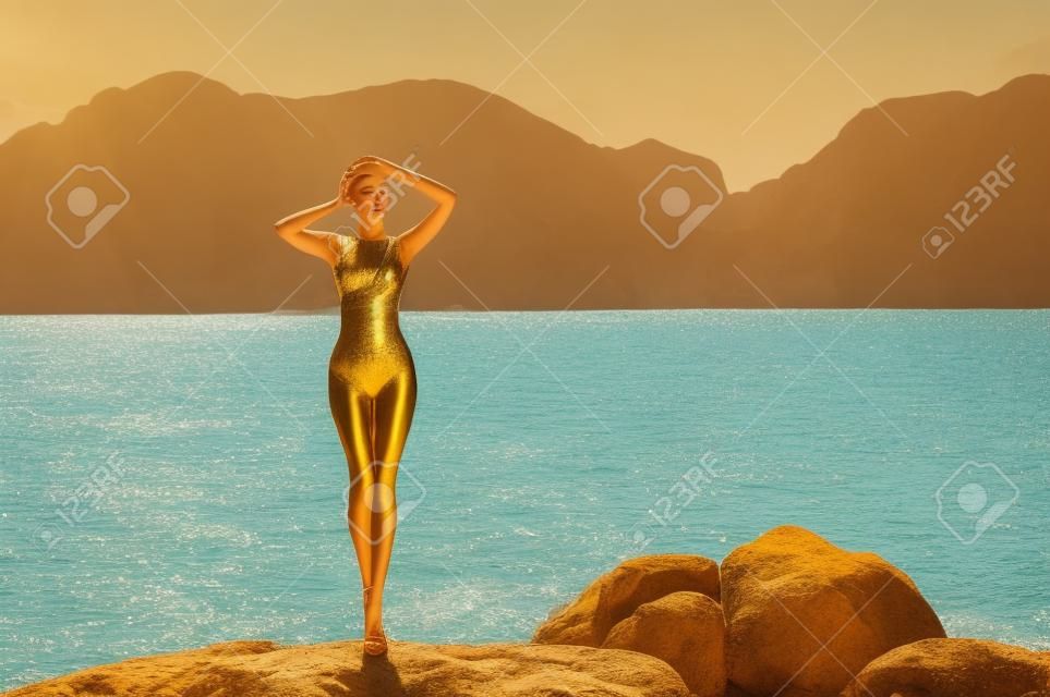 Prachtige jonge dame in een gouden badpak aan zee