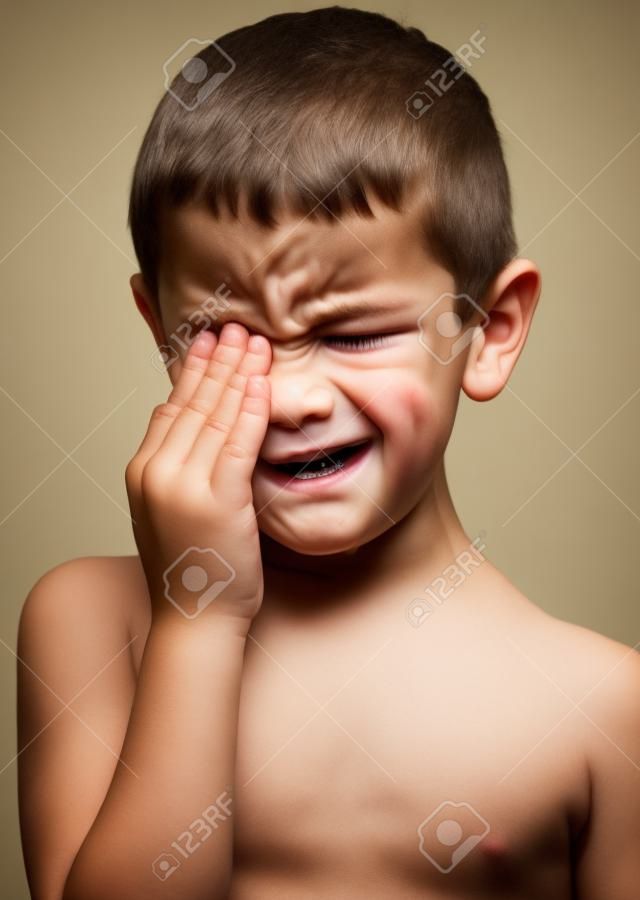 Portrait of boy crying, hands on face.