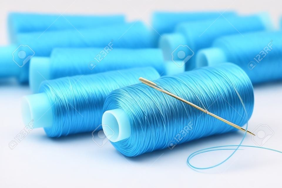 Many coils with threads of pastel tones. Coil of blue threads with large needle.