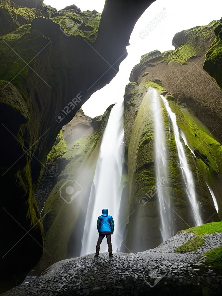 Glyufrafoss cachoeira no desfiladeiro das montanhas. Atração turística Islândia. Homem turista em jaqueta azul de pé em uma pedra e olha para o fluxo de água caindo. Beleza na natureza