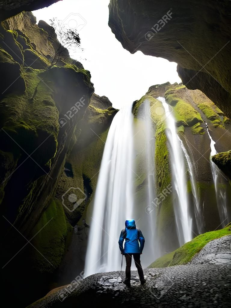 Glyufrafoss waterfall in the gorge of the mountains. Tourist Attraction Iceland. Man tourist in blue jacket standing on a stone and looks at the flow of falling water. Beauty in nature