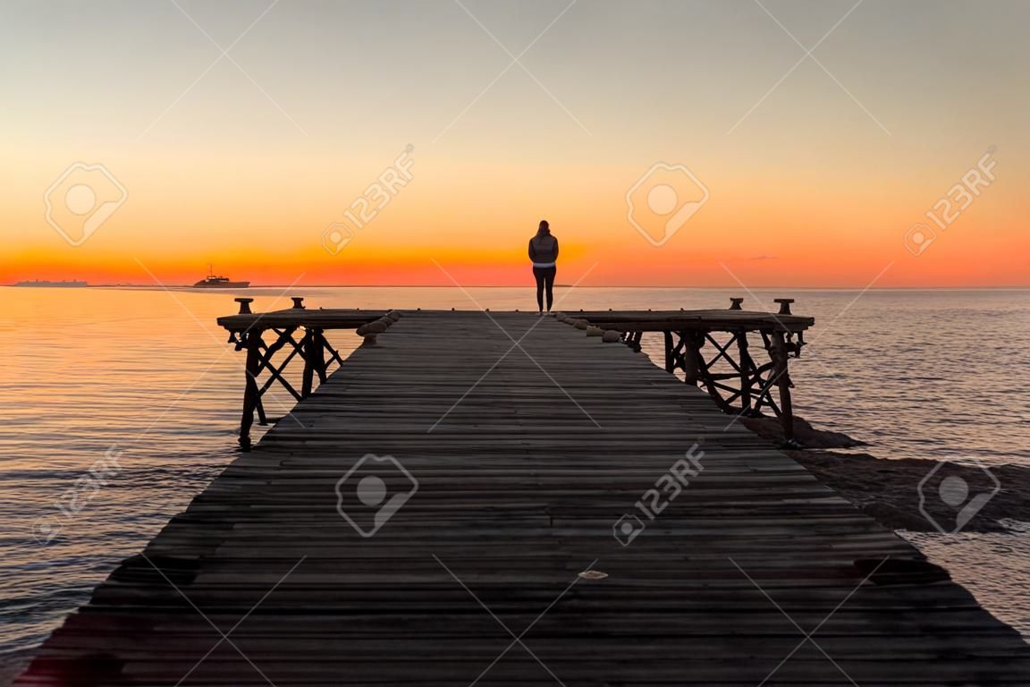 Femme seule debout sur la jetée au bord de la mer dans le paysage du lever du soleil d'été