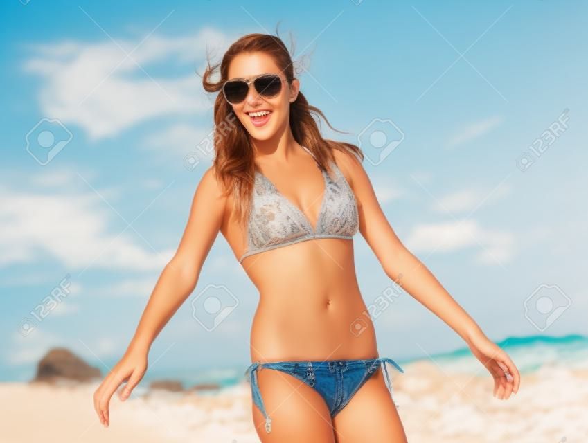 Schöne junge Frau, die mit einem ruhigen und glücklichen Gesichtsausdruck am Strand spazieren geht