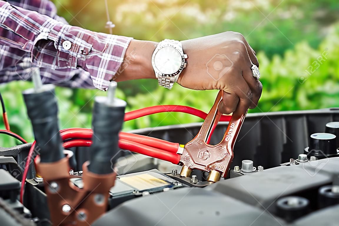 Close up hand of car technician holding cable to connect to battery,Car mechanic uses battery jumper cables charge a dead battery,A car mechanic uses battery jumper cables transferring power,spot focus.