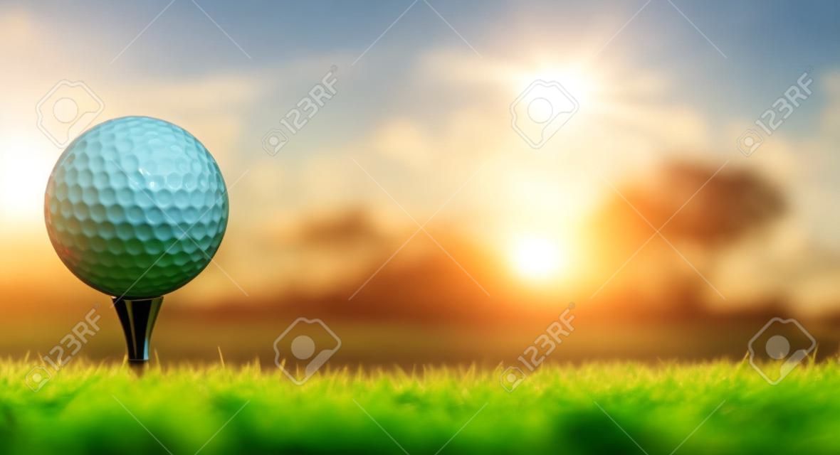 A golf ball on its tee in a green grass field golf course with sun rising.