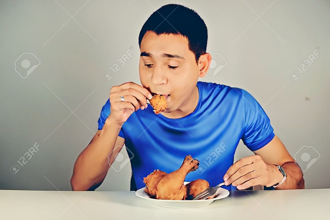 Joven comiendo pollo frito en la mesa, el tono de la vendimia