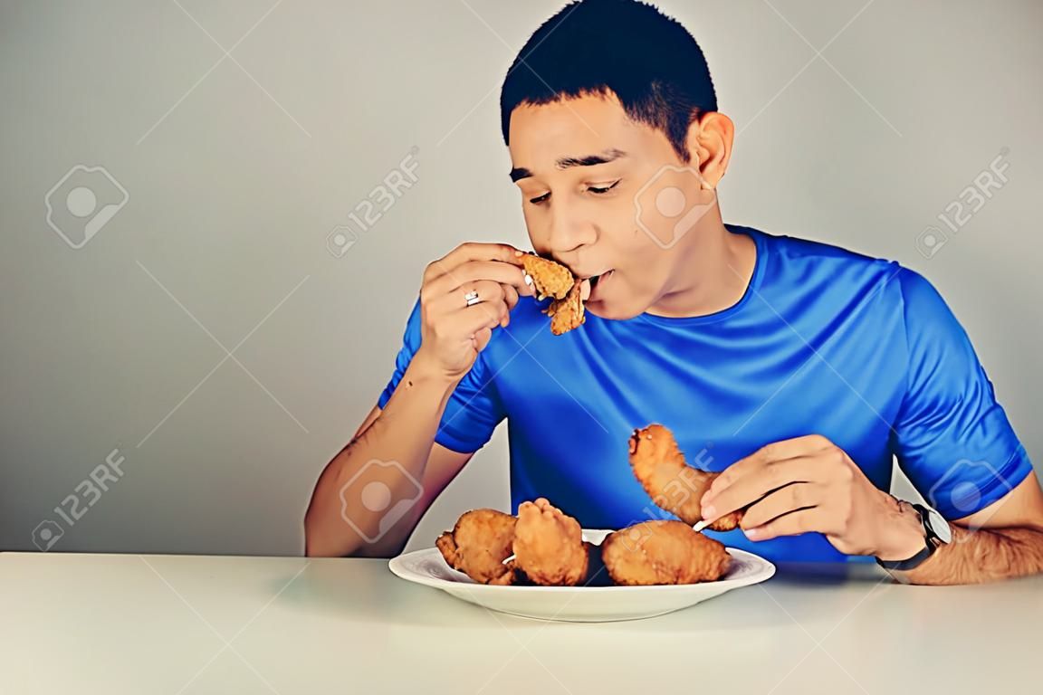 Joven comiendo pollo frito en la mesa, el tono de la vendimia