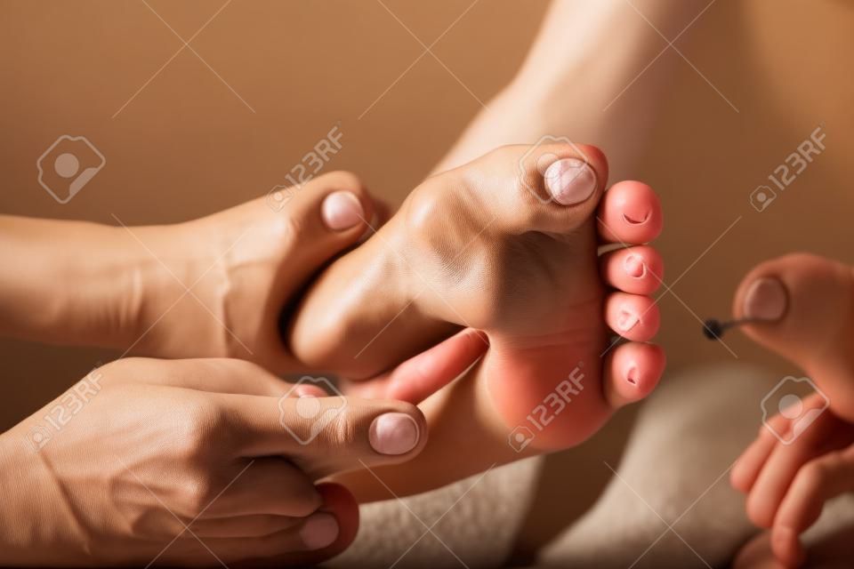 Professional therapist giving relaxing traditional thai reflexology foot massage with stick to a woman in spa