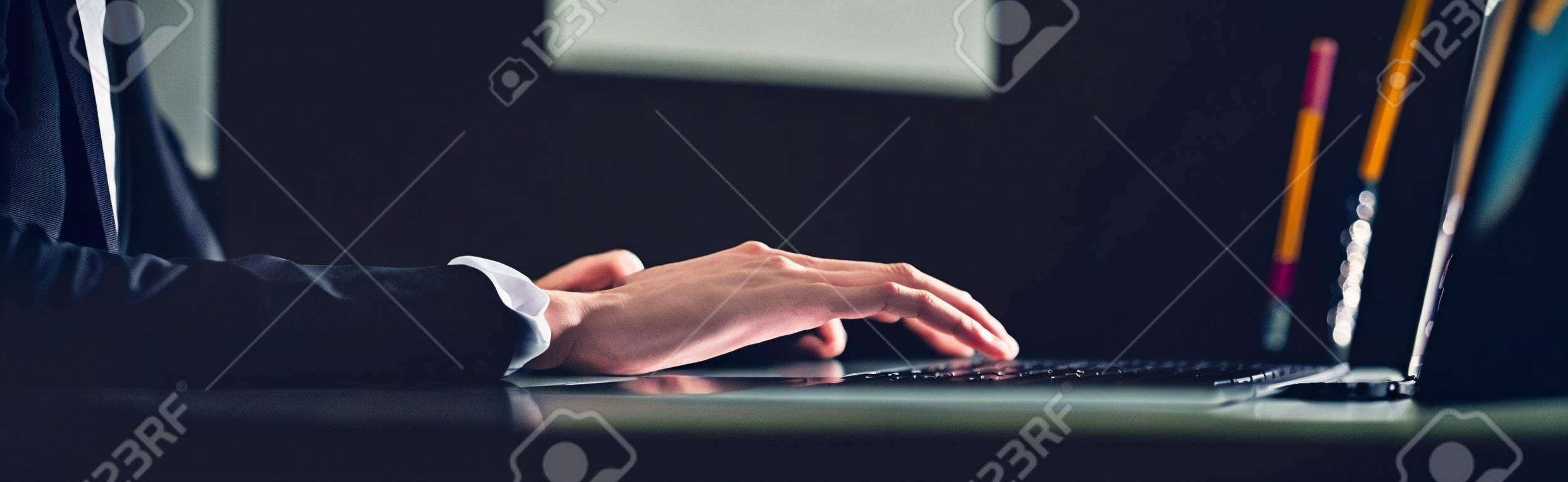 一名男子在深夜伏案办公时使用笔记本电脑处理新项目的想法——右边是一个带有复制空间的全景网络横幅。