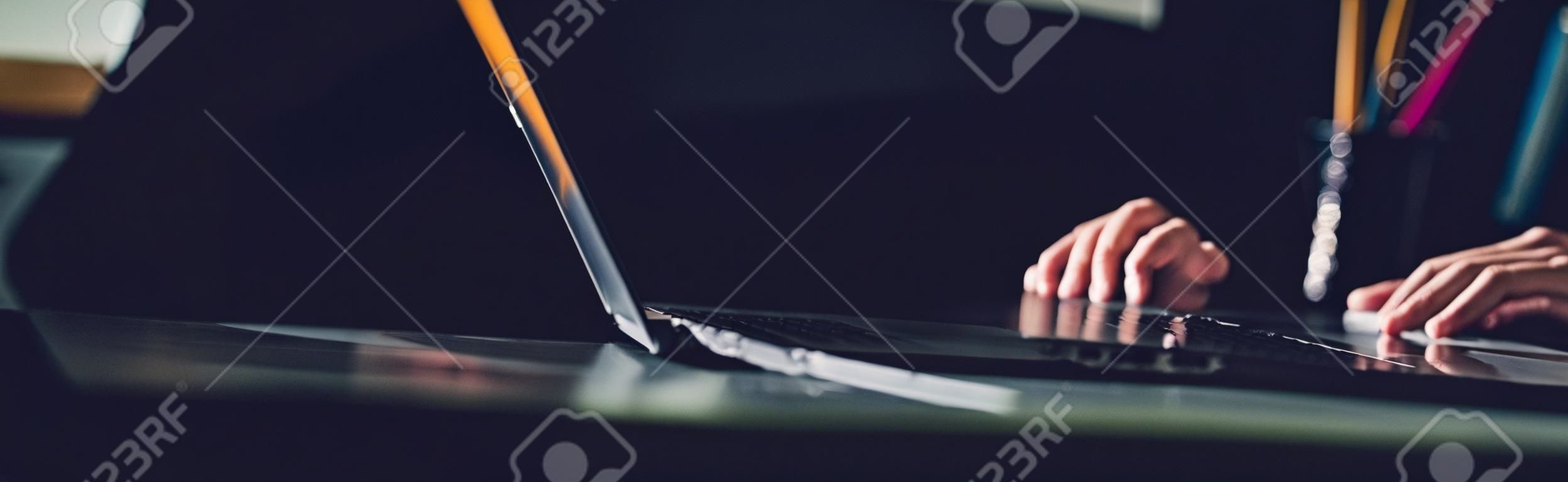 Un homme utilisant un ordinateur portable travaillant sur une nouvelle idée de projet à son bureau dans le bureau tard dans la nuit - bannière web panoramique avec espace copie sur la droite