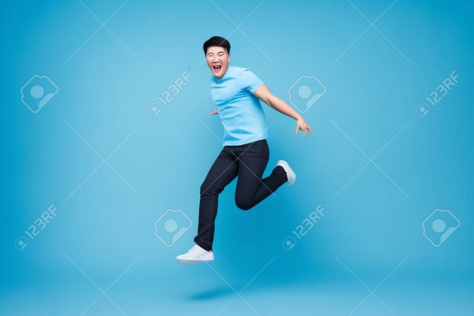 Energetic happy young Asian man in casual clothes jumping, studio shot isolated in light blue background