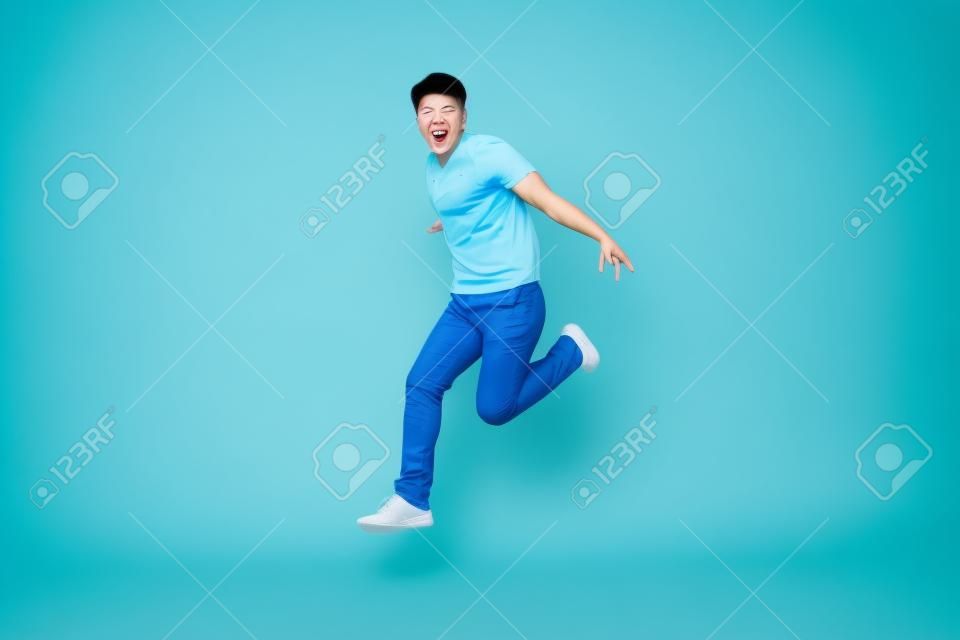 Energetischer glücklicher junger asiatischer Mann in Freizeitkleidung springen, Studioaufnahme einzeln in hellblauem Hintergrund