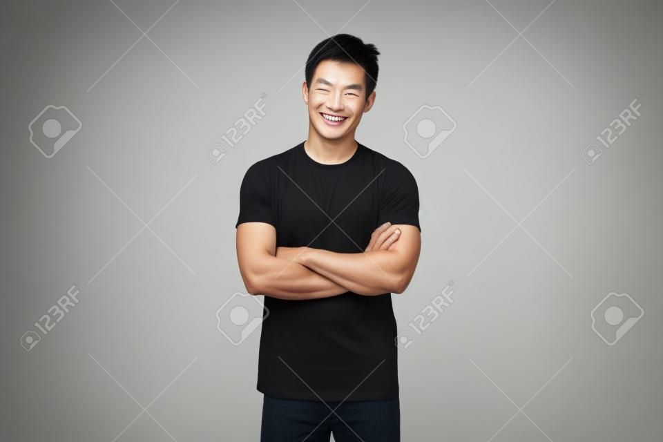 Sonriente hombre asiático guapo en camiseta negra casual con el brazo cruzado mirando a la cámara foto de estudio aislado sobre fondo blanco.