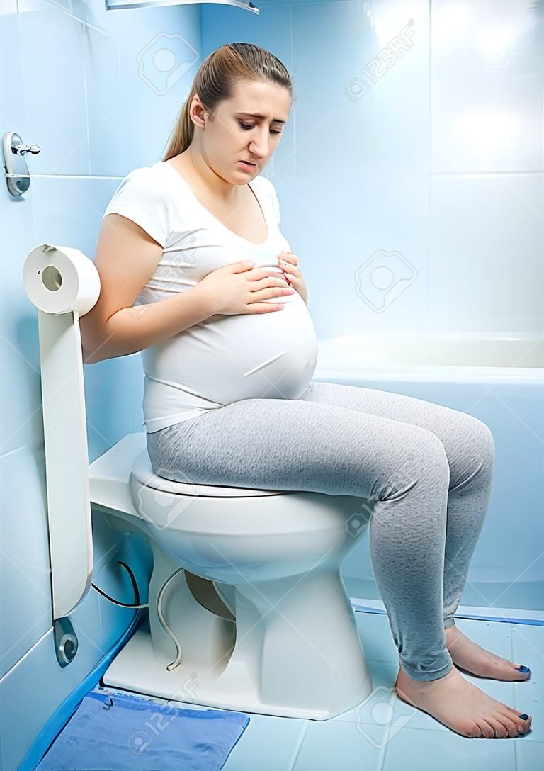 Jonge zieke zwangere vrouw witting op het toilet
