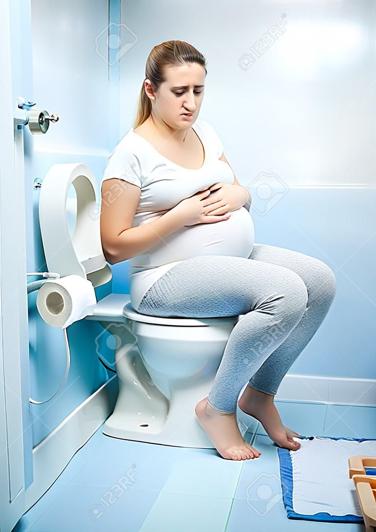 Jonge zieke zwangere vrouw witting op het toilet