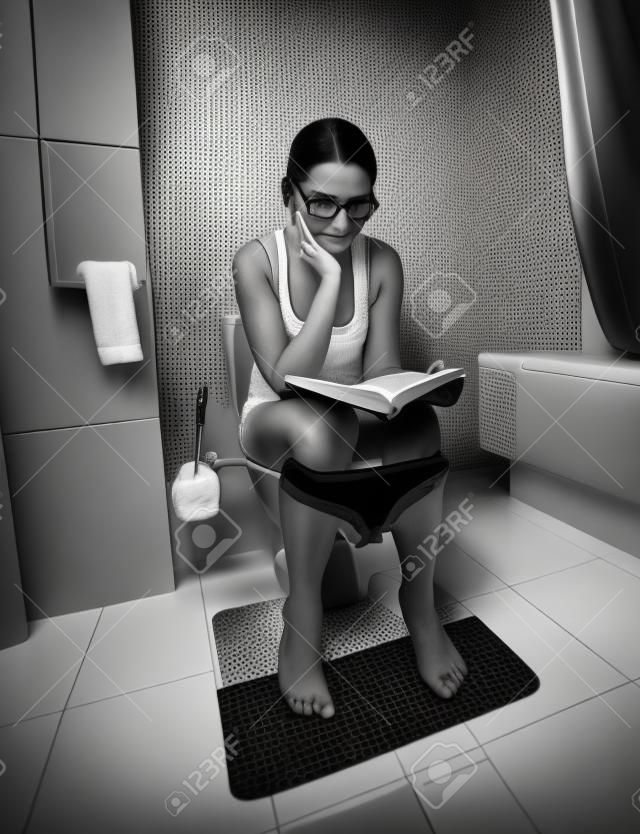 화장실 및 독서 책에 앉아 갈색 머리 여자의 흑백 이미지