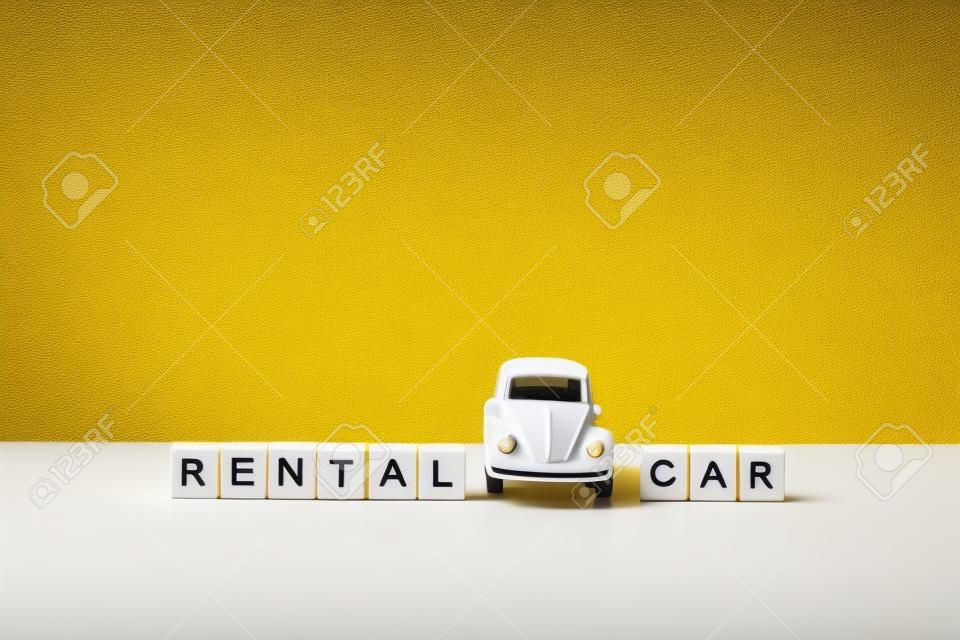 黄色の背景、木製のブロックの碑文と白いテーブルの上のおもちゃの白い車。レンタカーとカーシェアリングのコンセプト。