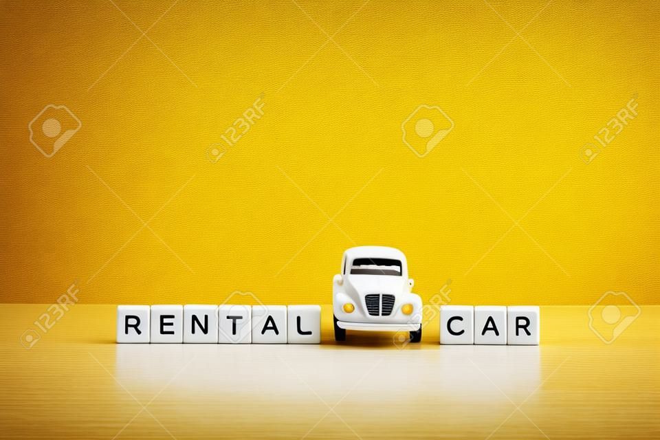 黄色の背景、木製のブロックの碑文と白いテーブルの上のおもちゃの白い車。レンタカーとカーシェアリングのコンセプト。