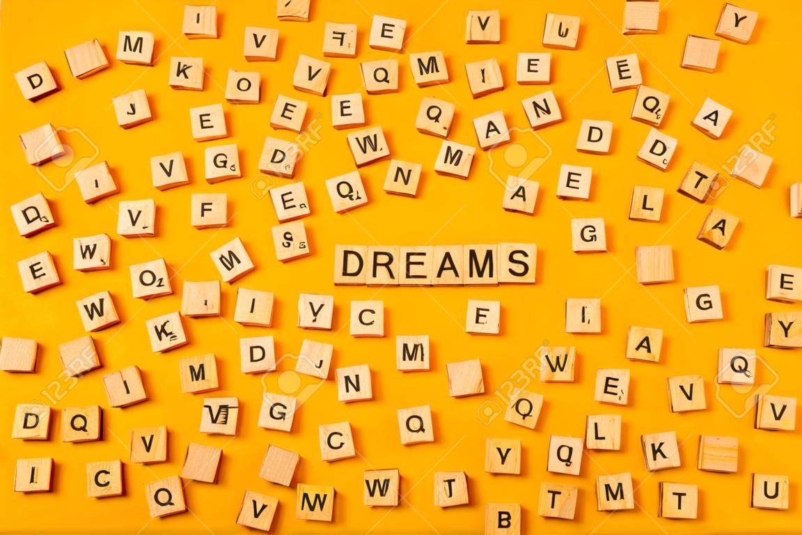 Das Wort "DREAMS" besteht aus Holzbuchstaben auf einem leuchtend gelben Hintergrund neben einer Reihe anderer Buchstaben. Motivationswörter Zitate Konzept