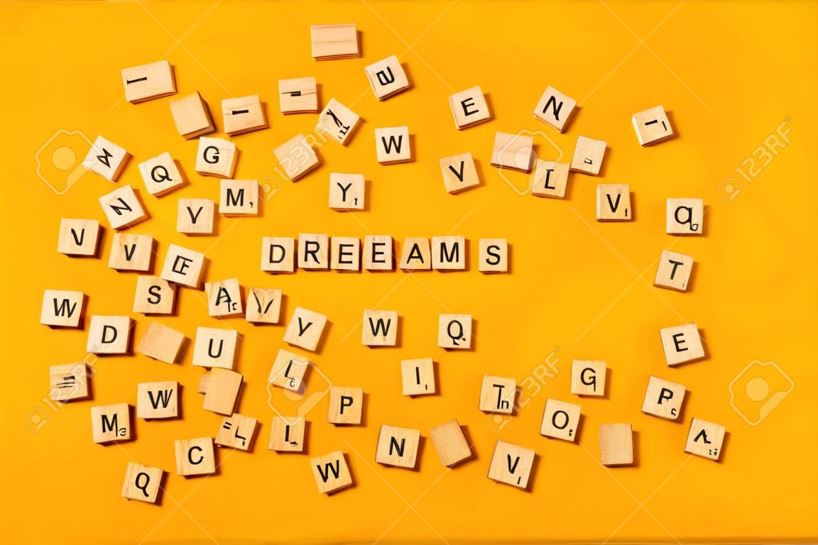 La palabra "SUEÑOS" está hecha de letras de madera sobre un fondo amarillo brillante junto a un montón de otras letras. Concepto de citas de palabras motivacionales
