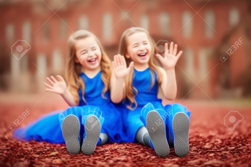 Two little girls sitting on the ground and showing their heels are laughing
